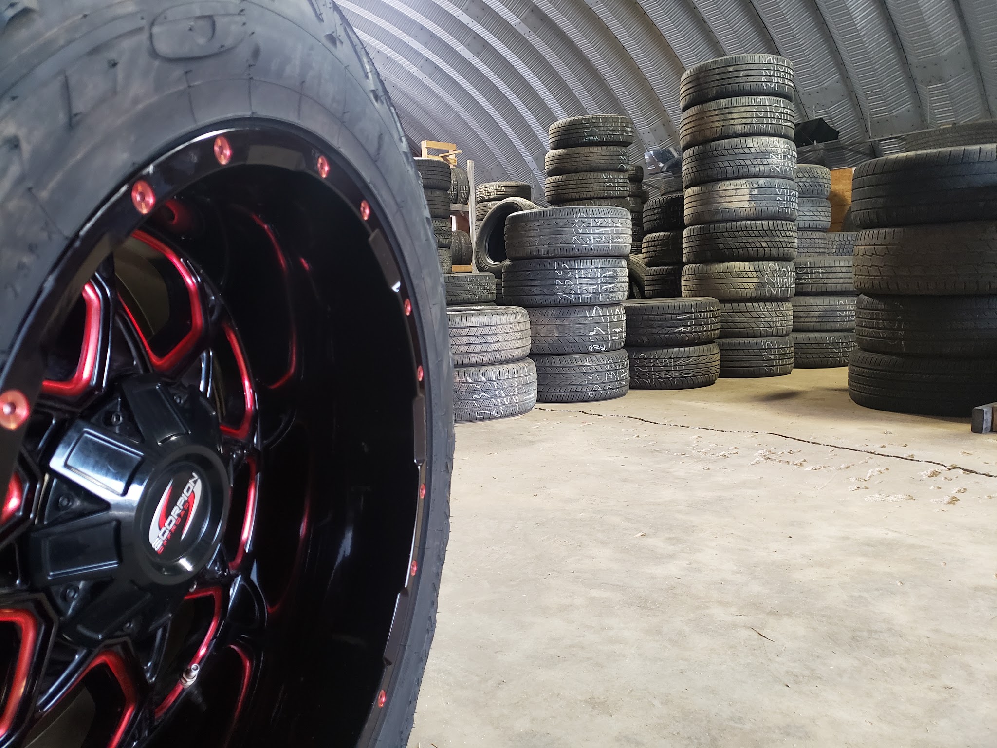 Stacks of used tires inside our shop beside a red and black wheel